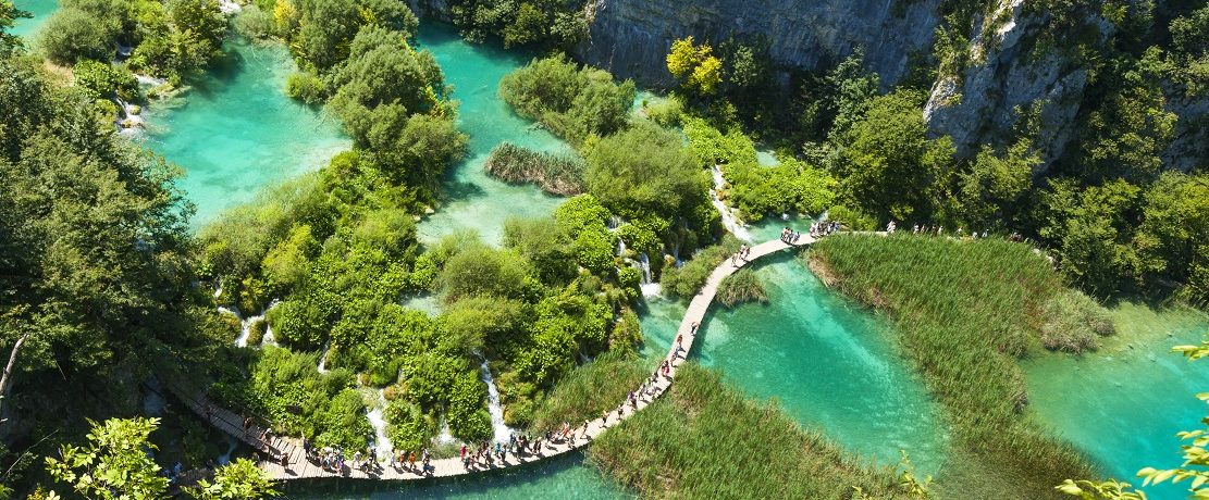 Tourists go on special tracks around the lake in the park Plitvice Lakes, Croatia. Plitvice Lakes - National Park in Croatia, located in the central part of the country. Since 1979, the national park "Plitvice Lakes" is included in the register of "World Heritage" by UNESCO. Initially, the park was not available to visitors, but were subsequently built wooden walkway and ecological transport running on electricity. Plitvice lakes are very popular among tourists.